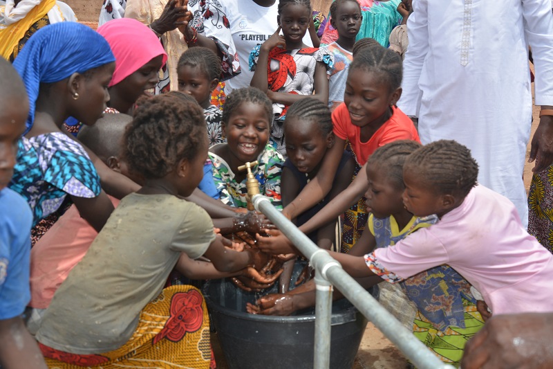 Laughing children washing hands around a water well