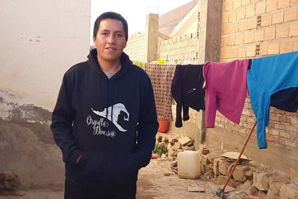 A young man stands outdoors in front of a brick wall and a clothesline in Bolivia.