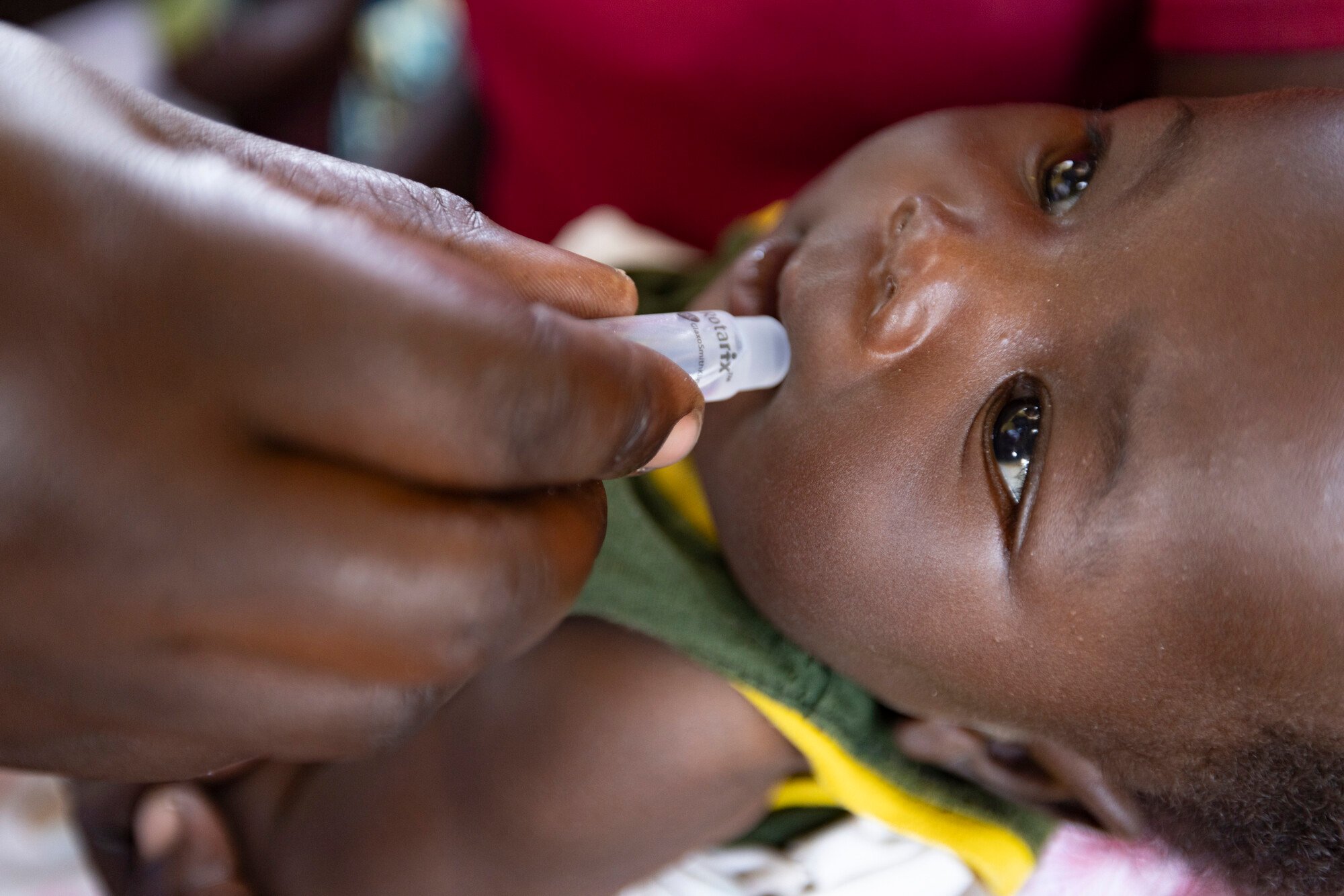 A baby lying down receives an oral dose of medicine from a caregiver’s hand, focusing on child healthcare.