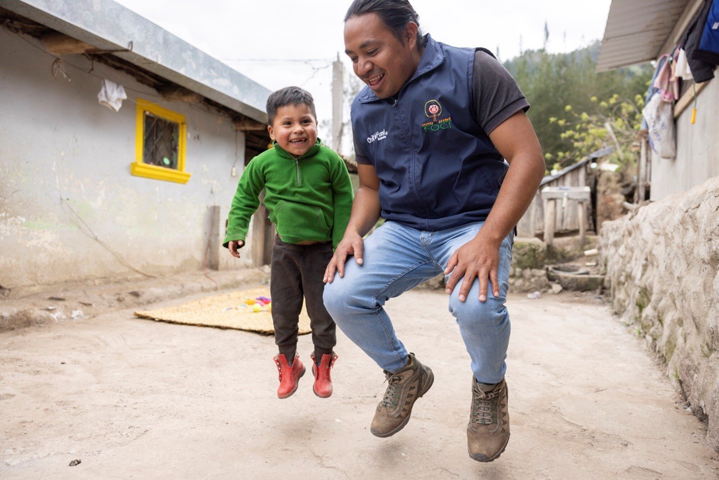 Child and community worker jumping together, symbolizing joy and local partnerships.