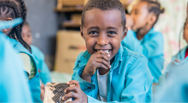 Smiling young boy in a blue school uniform enjoying a meal, symbolizing nourishment and education.