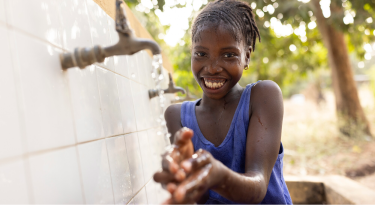 Smiling girl washing her hands under a water tap, symbolizing clean water access and hygiene.