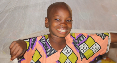 Smiling child under a mosquito net, representing health protection and well-being.