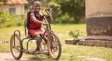 Smiling boy using a hand-powered tricycle, representing mobility and empowerment.