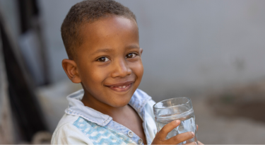 Smiling young boy holding a glass of clean water, representing health and safe water access.