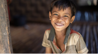 Smiling young boy sitting in a rustic wooden home, symbolizing resilience and hope.