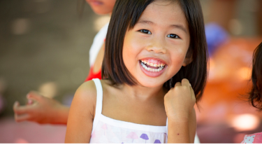 Smiling young girl laughing in an outdoor setting, symbolizing joy and childhood happiness.