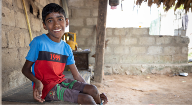 Smiling young boy with a disability sitting outside his rural home, symbolizing resilience and determination.