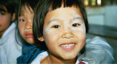 Smiling child with thanaka paste on their face, representing cultural tradition and joy.
