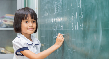 Young girl writing math equations on a chalkboard, symbolizing confidence in education.