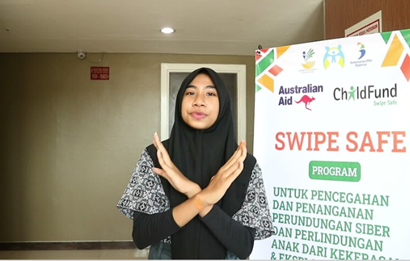A young woman in a black hijab stands in front of a ChildFund Swipe Safe program banner, crossing her arms in an "X" to signal rejection. The banner promotes online safety and cyberbullying prevention.